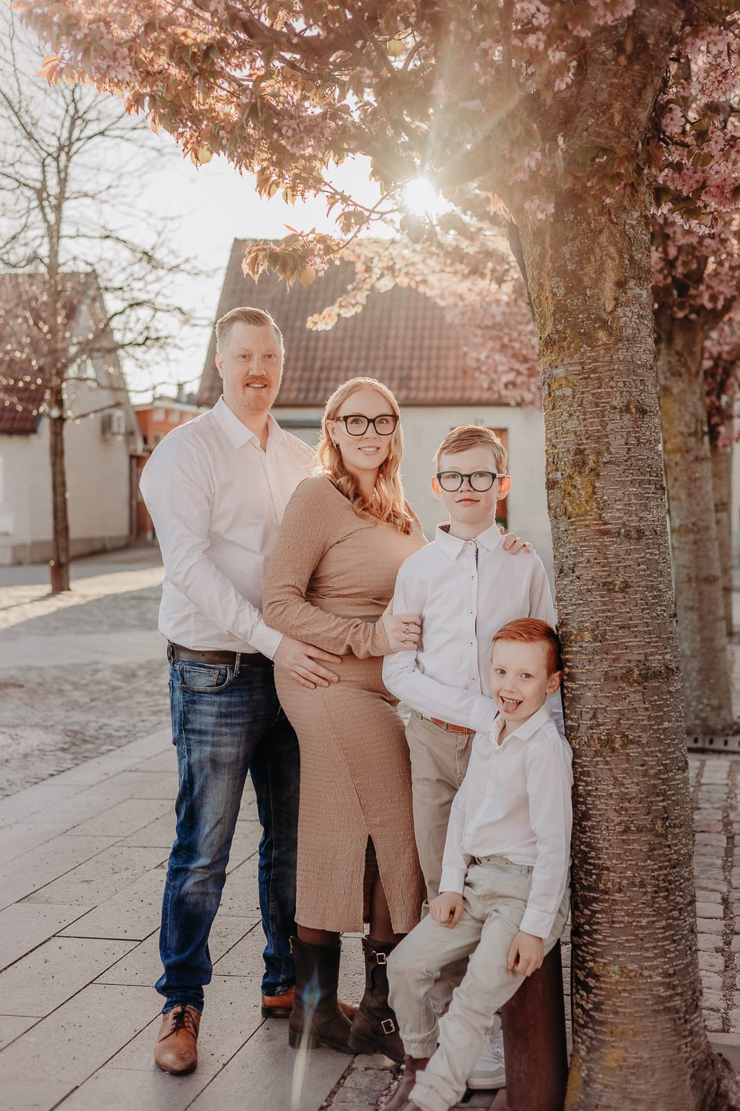 Familjefotografering i vårblomning – Familjefotograf Skåne Familj står tillsammans vid blommande träd vid en utomhusfotografering i Skåne med varmt kvällsljus