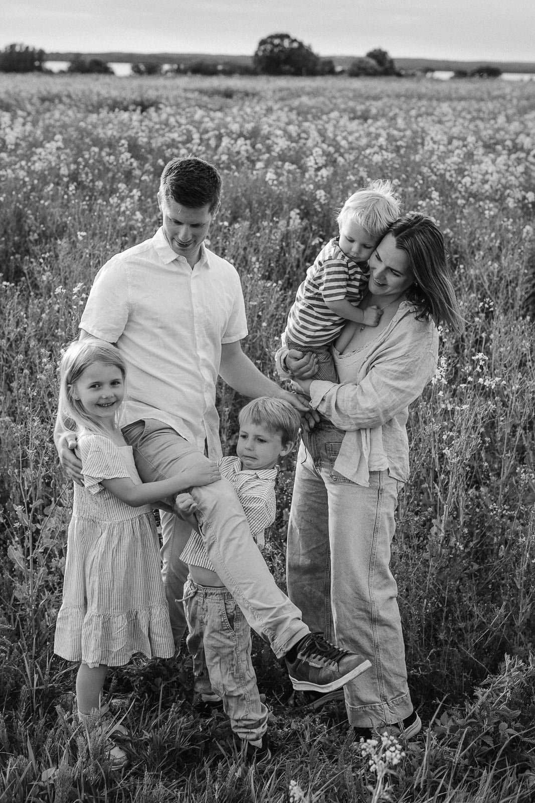 Tidlös familjefotografering i Skåne i mjukt kvällsljus&R_7-2 Familj med två barn går tillsammans på en grusväg i öppet landskap under solnedgång vid en naturlig familjefotografering i Skåne